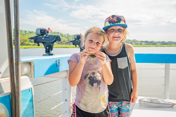 Two children smiling on a boat, one holding a small crab.