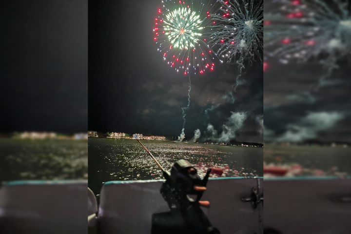 Fireworks over a lake at night, viewed from a boat with a railing.